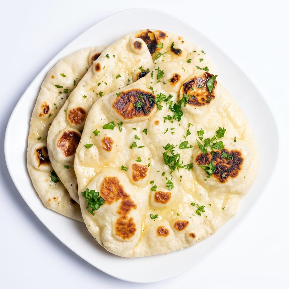 Three pieces of golden-brown naan bread, garnished with fresh parsley, on a white plate.