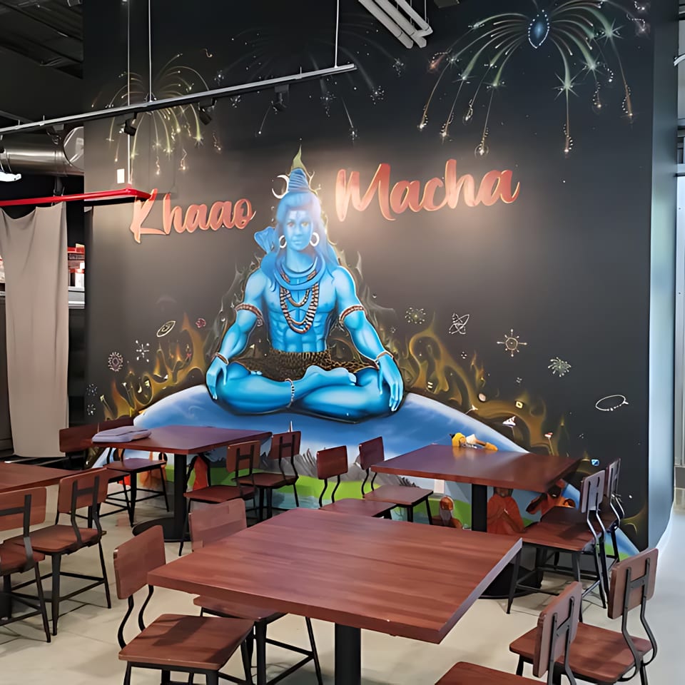 Restaurant interior with a large mural of a blue deity, wooden tables, and chairs.
